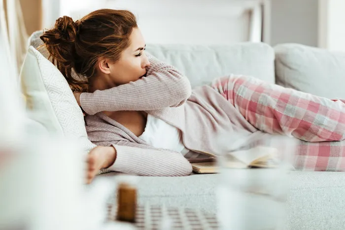 young-woman-coughing-into-elbow-while-lying-down-sofa-living-room